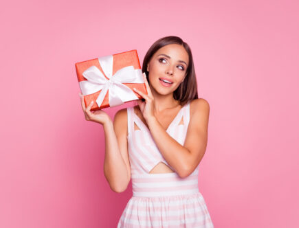 Foto einer jungen Dame, gekleidet in Sommerkleidung, die ein Geschenk hält und neugierig auf dessen Inhalt ist.