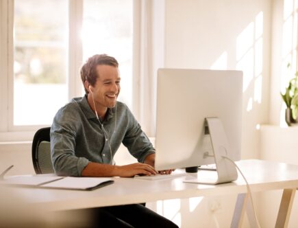 Ein Mann arbeitet lächelnd an einem Computer im Home Office, unterstützt durch Akustikpaneele zur Schallreduzierung
