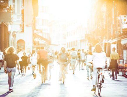 Menschen spazieren und fahren Fahrrad entlang einer belebten Einkaufsstraße in München bei Sonnenuntergang
