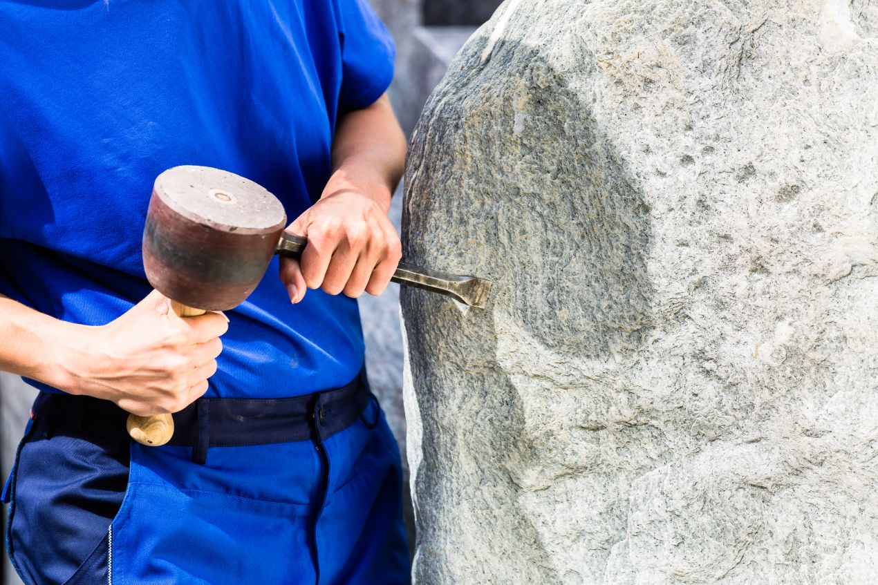 Handwerker bearbeitet Felsen mit Hammer und Meißel – professionelle Steinbearbeitung für Garten- und Landschaftsgestaltung.