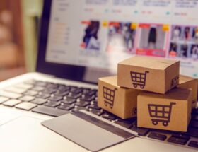 Symbolbild fuer Damenmode online kaufen mit Versandkartons auf Laptop und geoeffnetem Onlineshop im Hintergrund