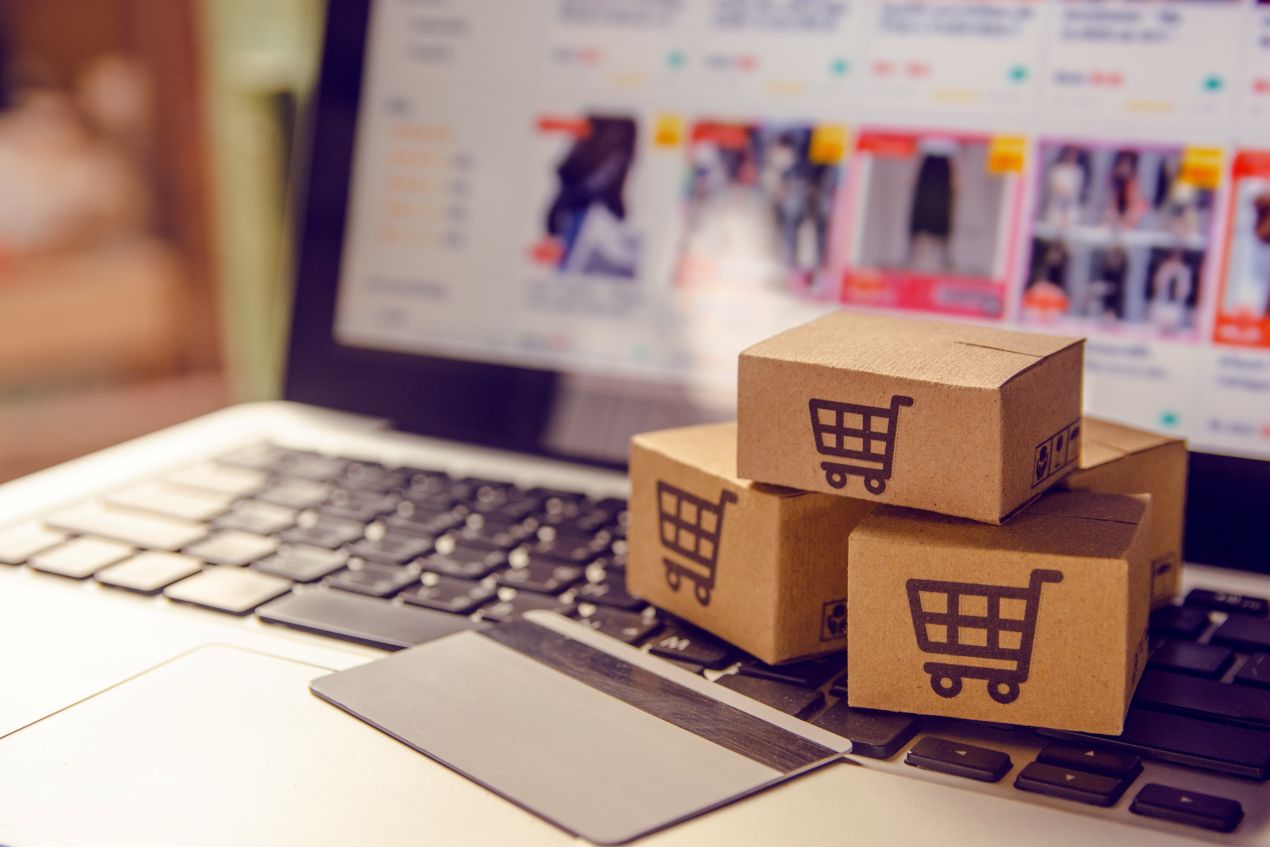 Symbolbild fuer Damenmode online kaufen mit Versandkartons auf Laptop und geoeffnetem Onlineshop im Hintergrund