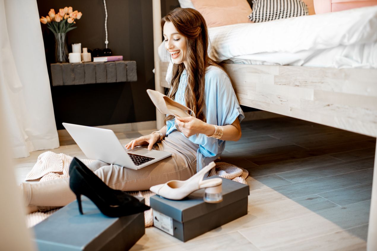 Junge Frau sitzt auf dem Boden und testet Schuhe beim Damenmode online kaufen mit Laptop