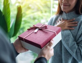 Person überreicht ein rotes Geschenk mit Schleife – ideale Szene für persönliche Geschenkideen wie ein Handtuch mit Namen