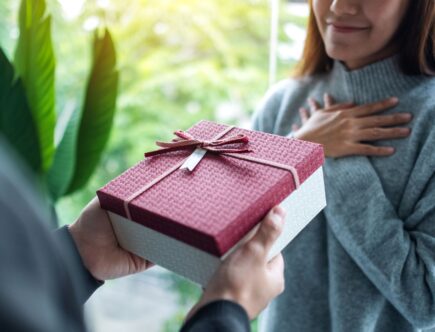 Person überreicht ein rotes Geschenk mit Schleife – ideale Szene für persönliche Geschenkideen wie ein Handtuch mit Namen