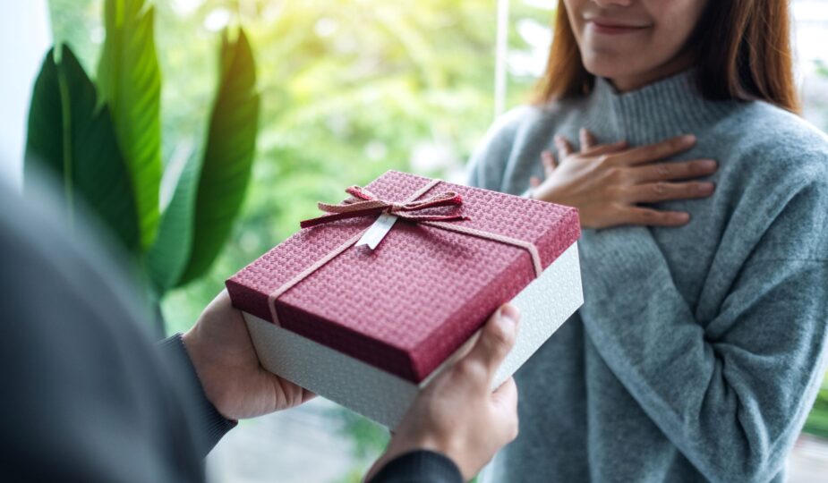 Person überreicht ein rotes Geschenk mit Schleife – ideale Szene für persönliche Geschenkideen wie ein Handtuch mit Namen
