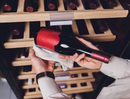 Person wählt Weinflasche im Regal aus