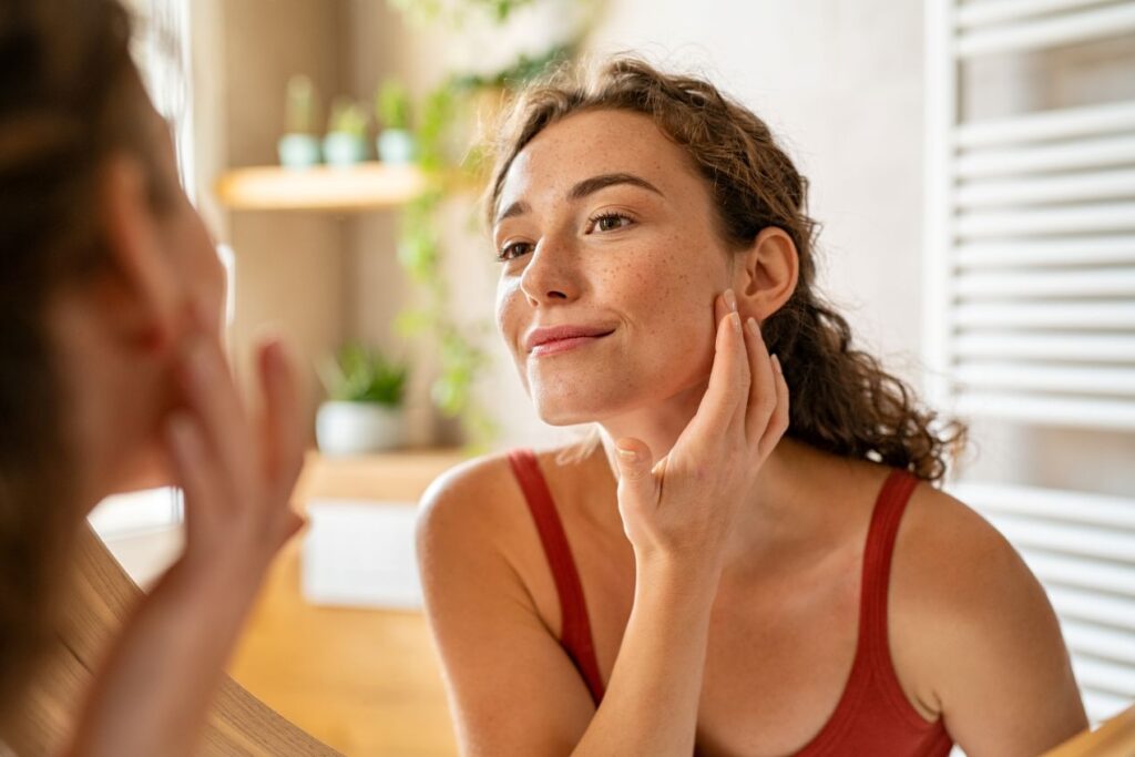 Nach der Haarentfernung in Duesseldorf kontrolliert eine Frau zufrieden ihre klare Haut im Spiegel – ohne Make-up oder Zusatzprodukte.