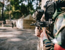 Spieler mit Paintball Waffe hinter Deckung im Wald waehrend eines Action-Matches