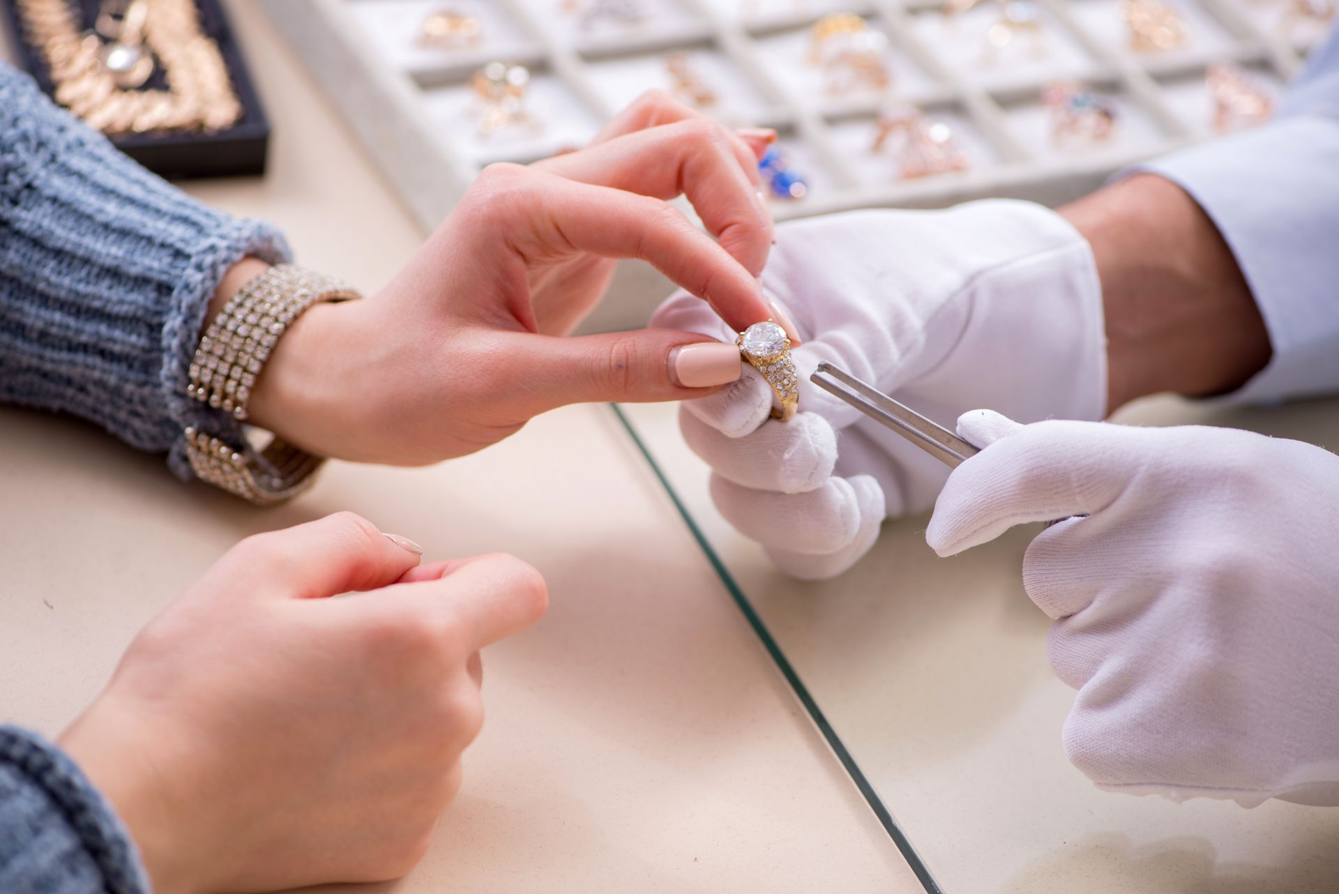 Kundin betrachtet einen Ring in einem Fachgeschaeft, Experte mit Handschuhen zeigt Details mit Pinzette, passend zum Shopping von Antik Schmuck