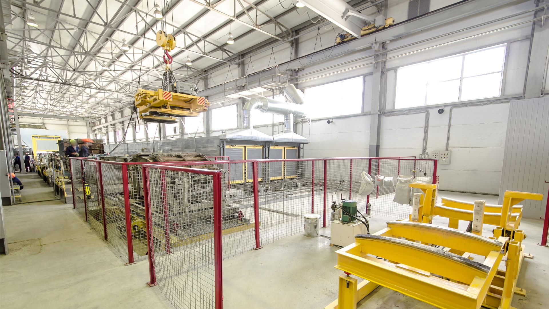 Industrielle Fertigungshalle mit laufendem Elektrokettenzug und Arbeiter